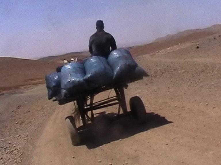 Man carrying coal bags on a rustic vehicle