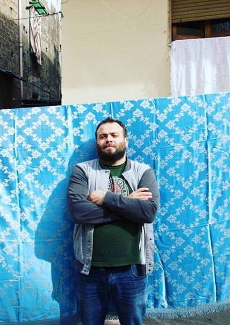 Gaetano Del Mauro standing with his arms crossed in front of a blue patterned blanked